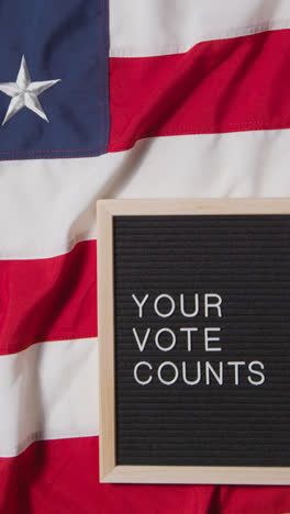 Vertical-Video-Of-Sign-Reading-Your-Vote-Counts-Lying-On-US-Stars-And-Stripes-Flag-For-American-Election-2024